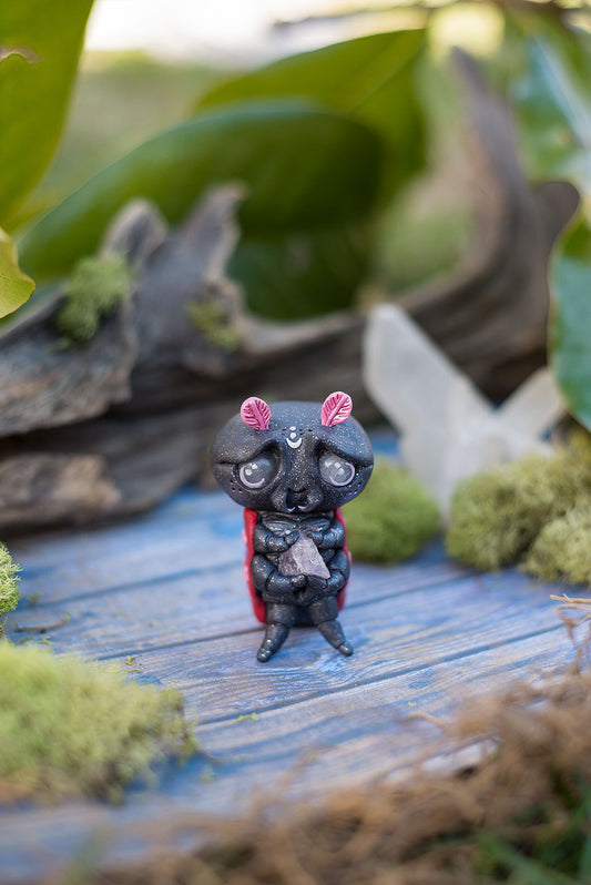 Front view of Amoura the love bug Mish - Hand sculpted red & black ladybug polymer clay creature, holding rose quartz