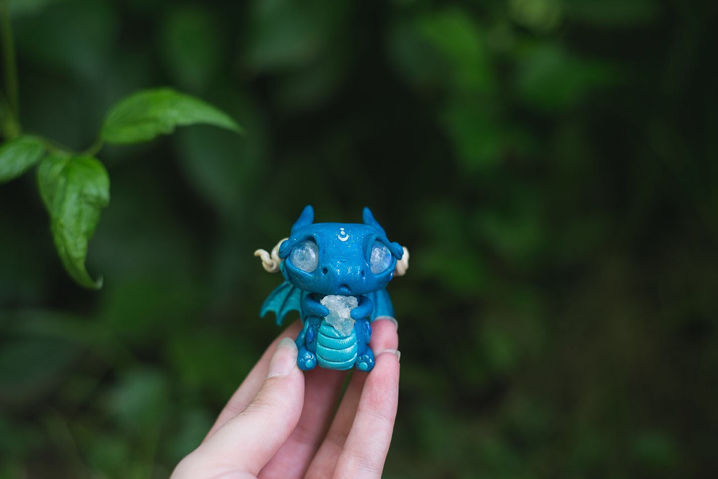 Size Comparison in Hand of Blue Dragon Mish - handmade polymer clay dragon creature with tail and wings, holding aquamarine crystal