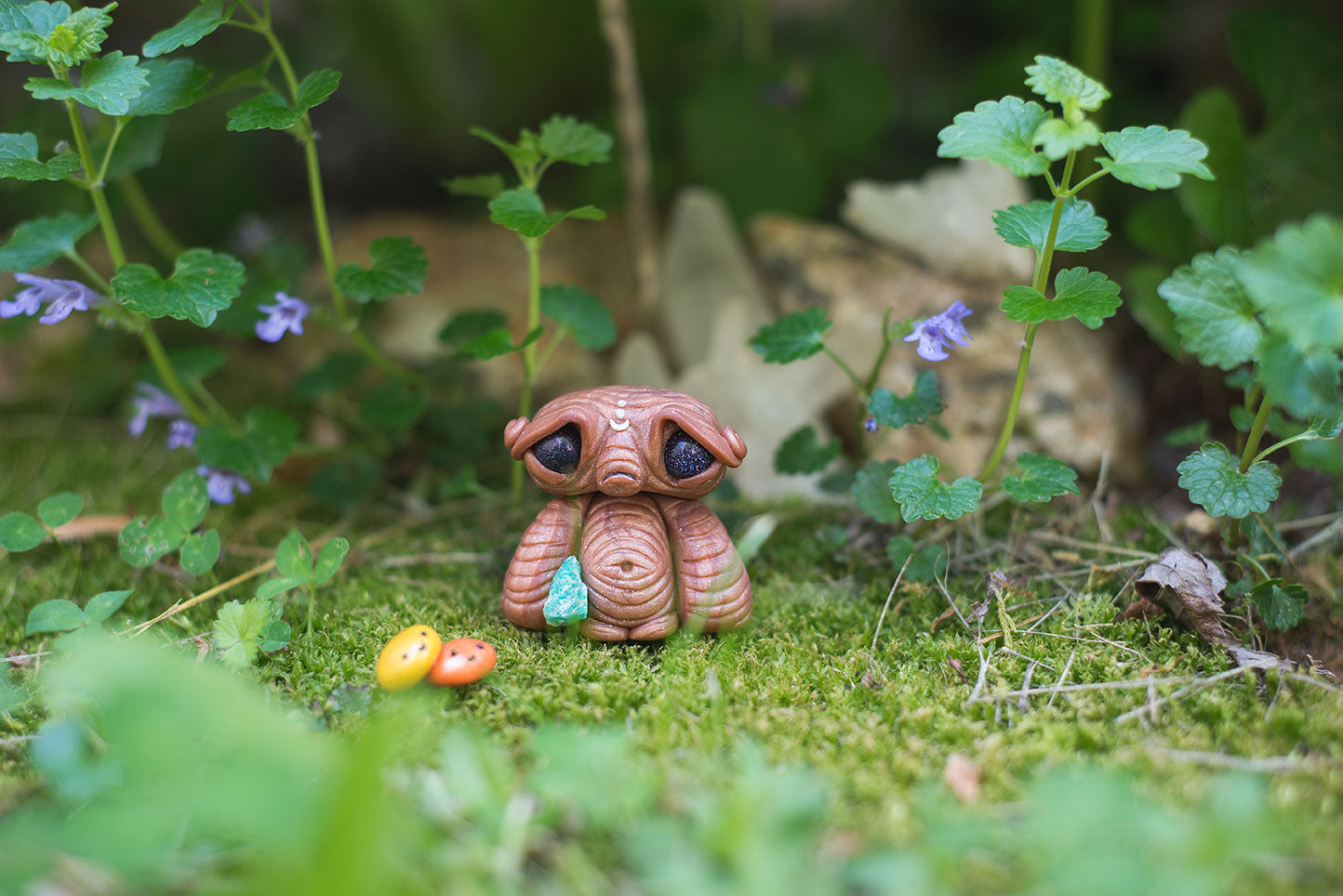 Custom hand sculpted polymer clay brown alien mish hiding in moss with galaxy eyes holding adventurine