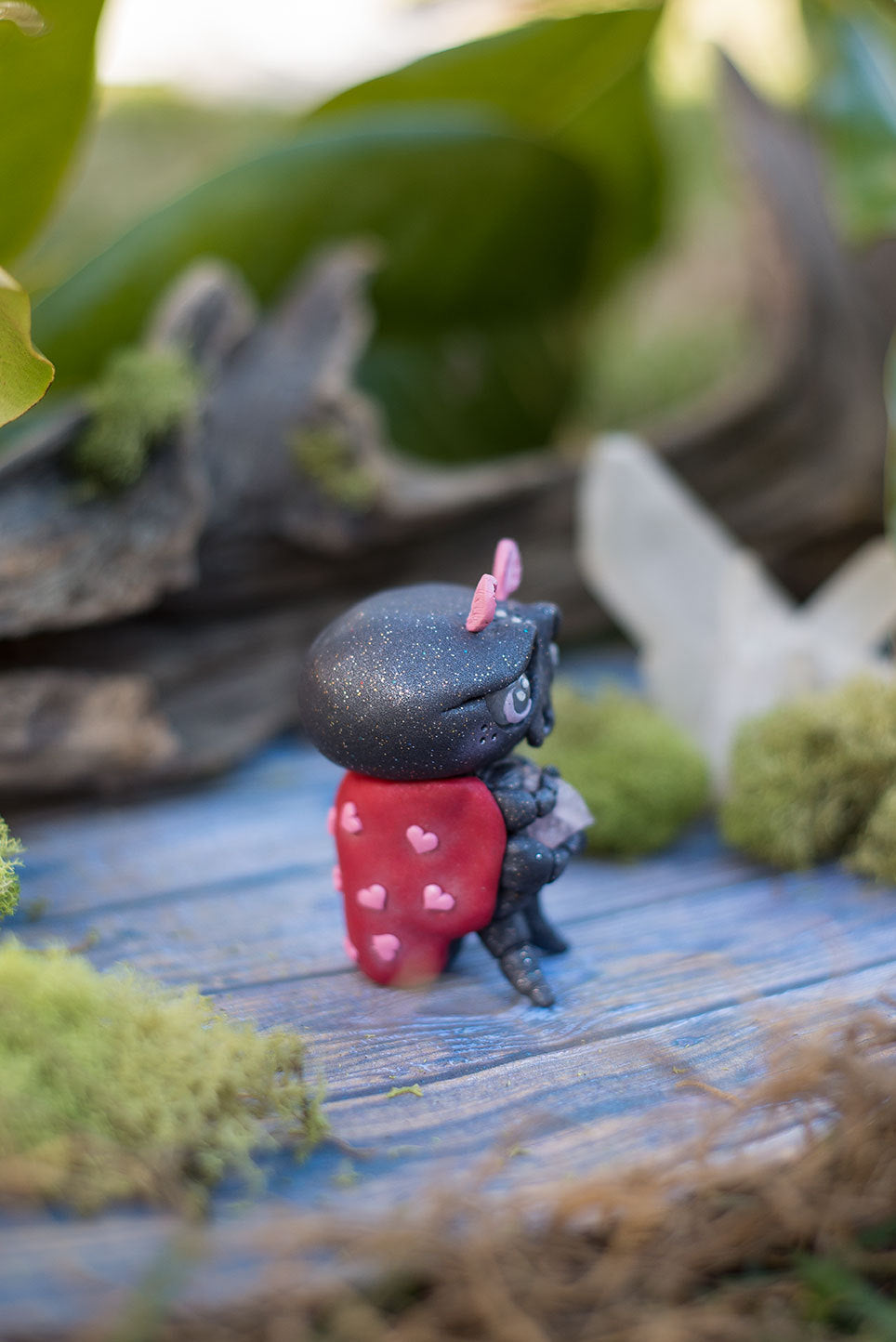 Side view of Amoura the love bug Mish - hand sculpted red and black ladybug polymer clay creature with pink hearts holding rose quartz