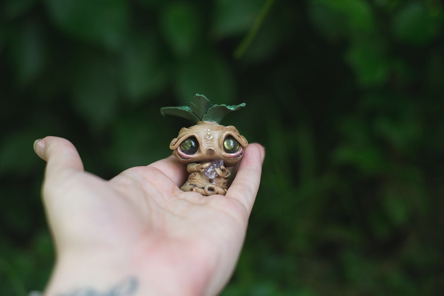 Size comparison in hand of Beige Mandrake Mish - handmade polymer clay mandragora root creature with holding fluorite
